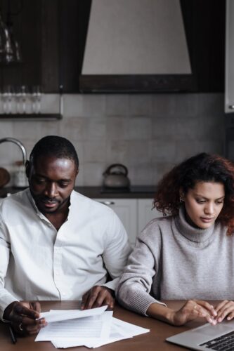 A couple works remotely on laptops and documents in their kitchen at home.
